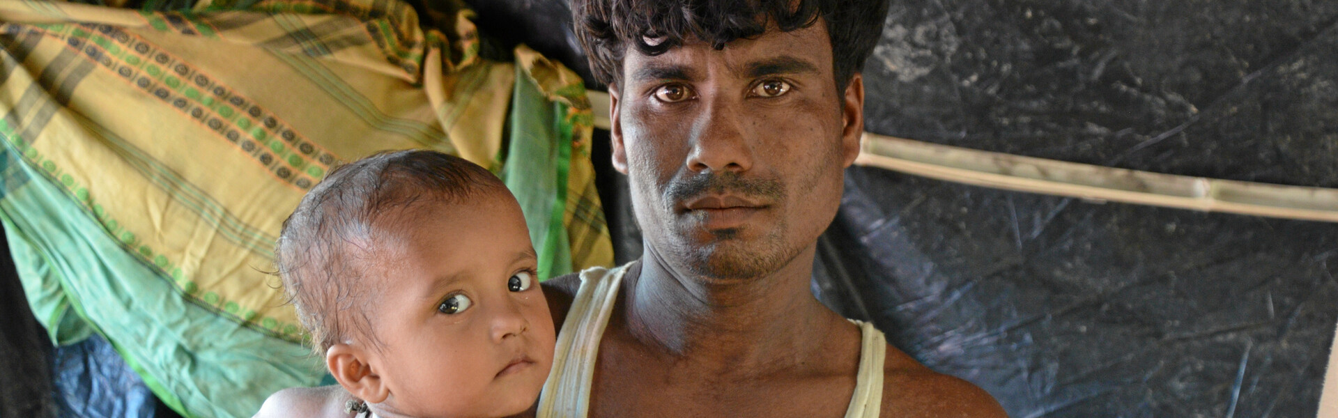 Ein Mann steht mit seinem Kind unter einem Zelt. Sie sind beide Rohingya-Flüchtlinge.
