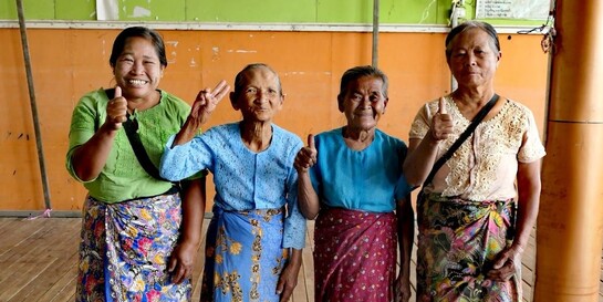 Vier Frauen, teilweise höheren Alters, lächeln und zeigen das Daumen-hoch-Zeichen oder Peace-Zeichen