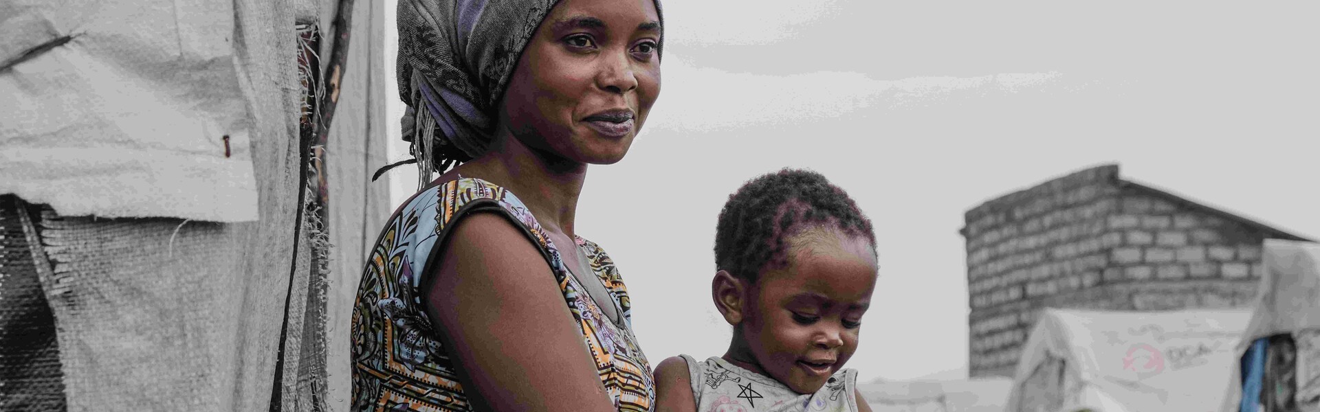 Eine Mutter mit ihrem Kleinkind auf dem Schoß, in der demokratischen Republik Kongo. Zelte im Hintergrund