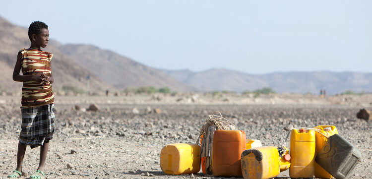 Ein Junge in Äthiopien steht neben Wasserkanistern