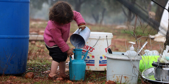 Ein Mädchen in einem syrischen Flüchtlingslager füllt sich Wasser in einen türkisfarbenen Krug