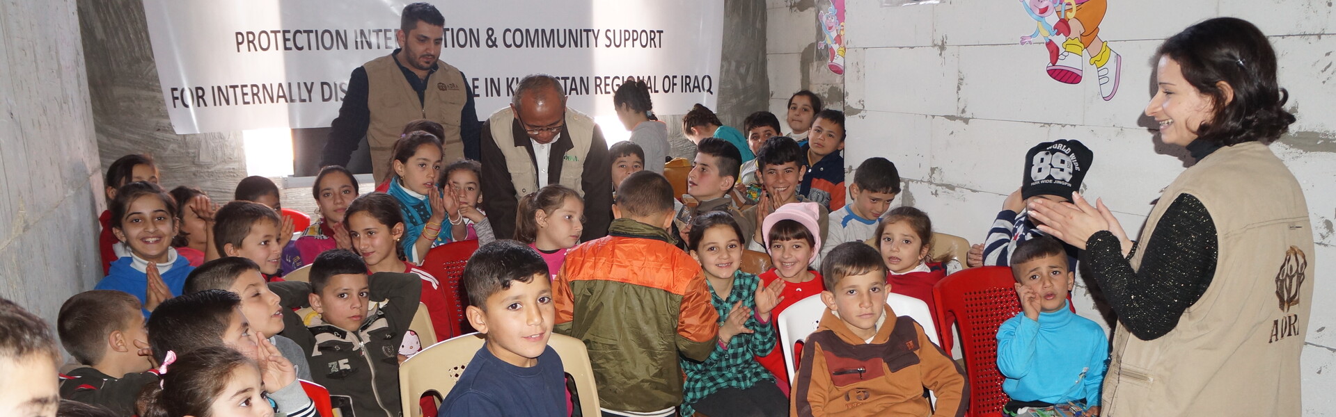 Kinder sitzen im Irak in einem Haus und eine Helferin unterhält sie. Die Kinder sind Opfer der Flüchtlingskrise.