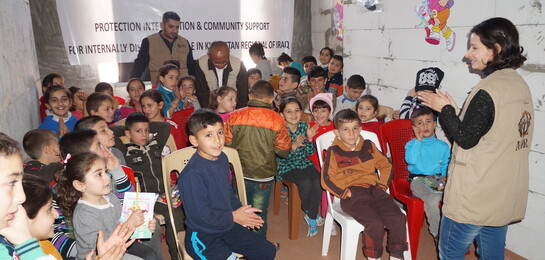 Kinder sitzen im Irak in einem Haus und eine Helferin unterhält sie. Die Kinder sind Opfer der Flüchtlingskrise.