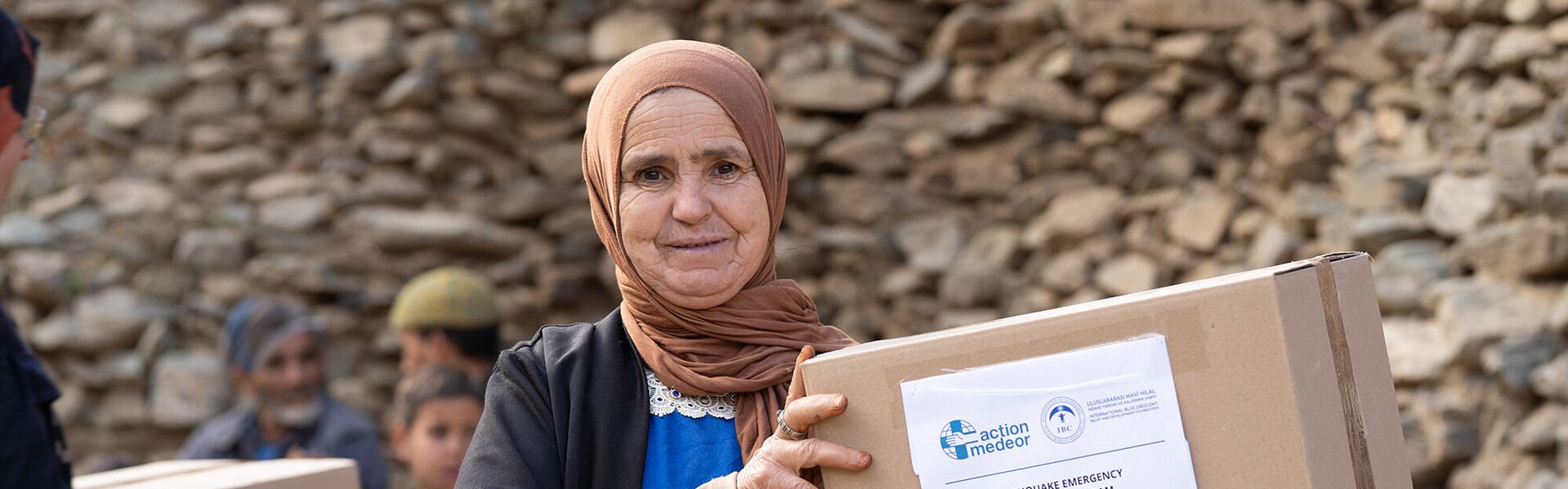 Eine Frau mit Kopftuch hält ein Paket mit einer Hilfslieferung von action medeor in der Hand