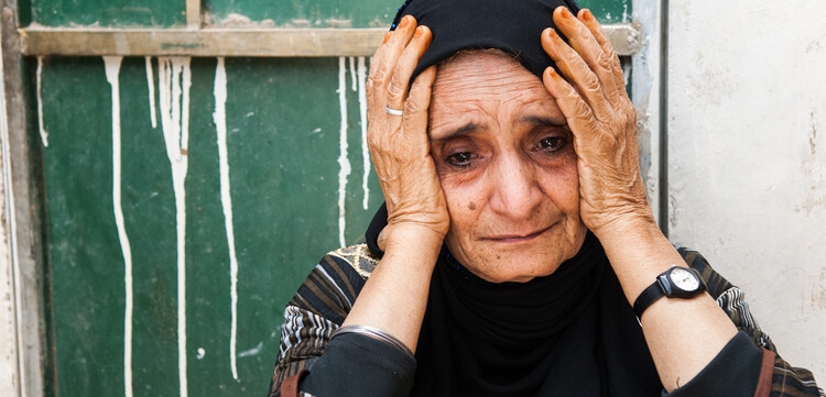 Eine ältere Frau im Jemen sitzt verzweifelt vor ihrem Haus