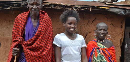 Janet und ihre Eltern in traditioneller Massai-Tracht stehen vor dem Haus in Kenia. 