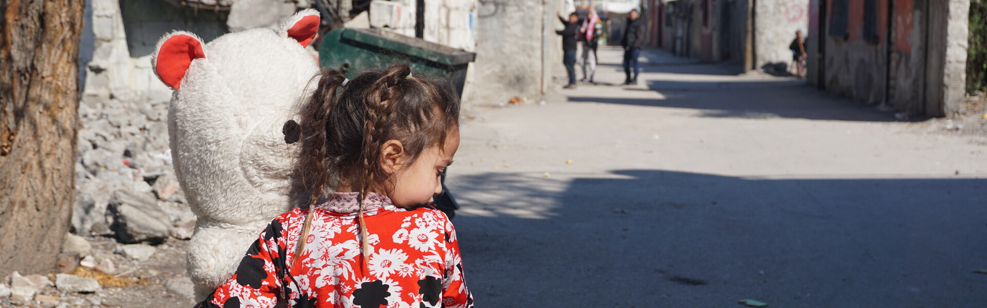 Ein Mädchen läuft mit einem großen Teddybären durch die Straßen in Syrien