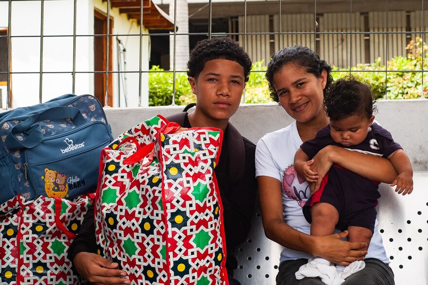 Eine Mutter sitzt mit ihrem jugendlichen Sohn und einem Baby nach dem Erdbeben in Venezuela auf einer Bank, neben ihnen stehen Klamottensäcke