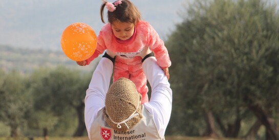 Eine Helferin hebt ein Kind hoch in die Luft