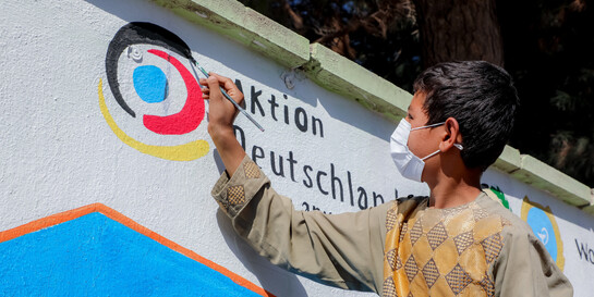 Ein Junge malt das Logo von Aktion Deutschland Hilft an eine Wand