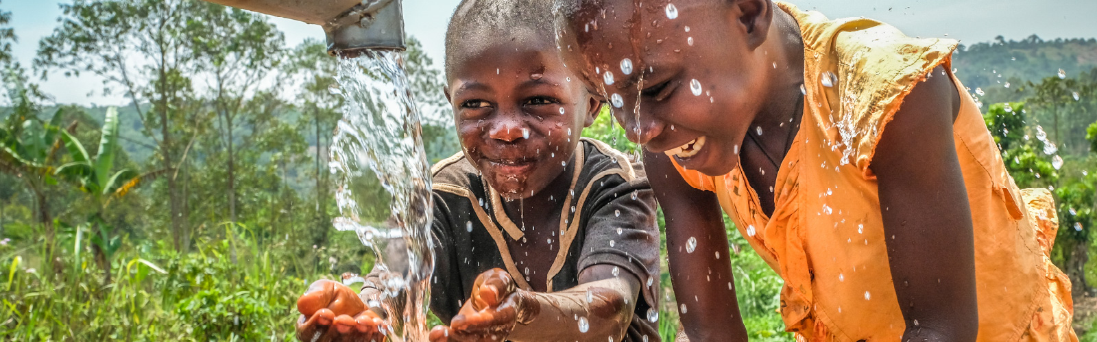 Zwei Kinder spielen mit Wasser an einem Brunnen