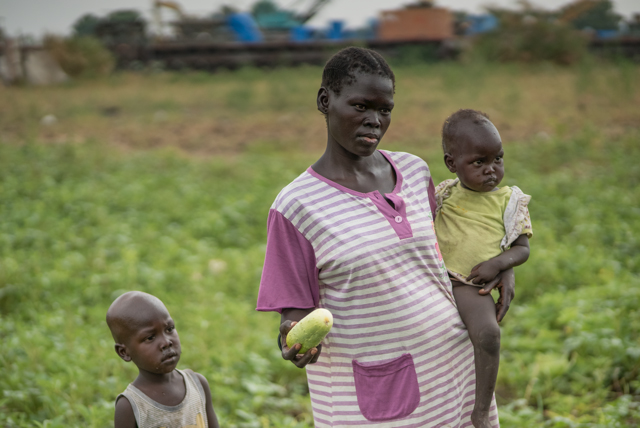 Mutter trägt ihr Kind im Südsudan über das Gurkenfeld Mutter trägt ihr Kind im Südsudan über das Gurkenfeld