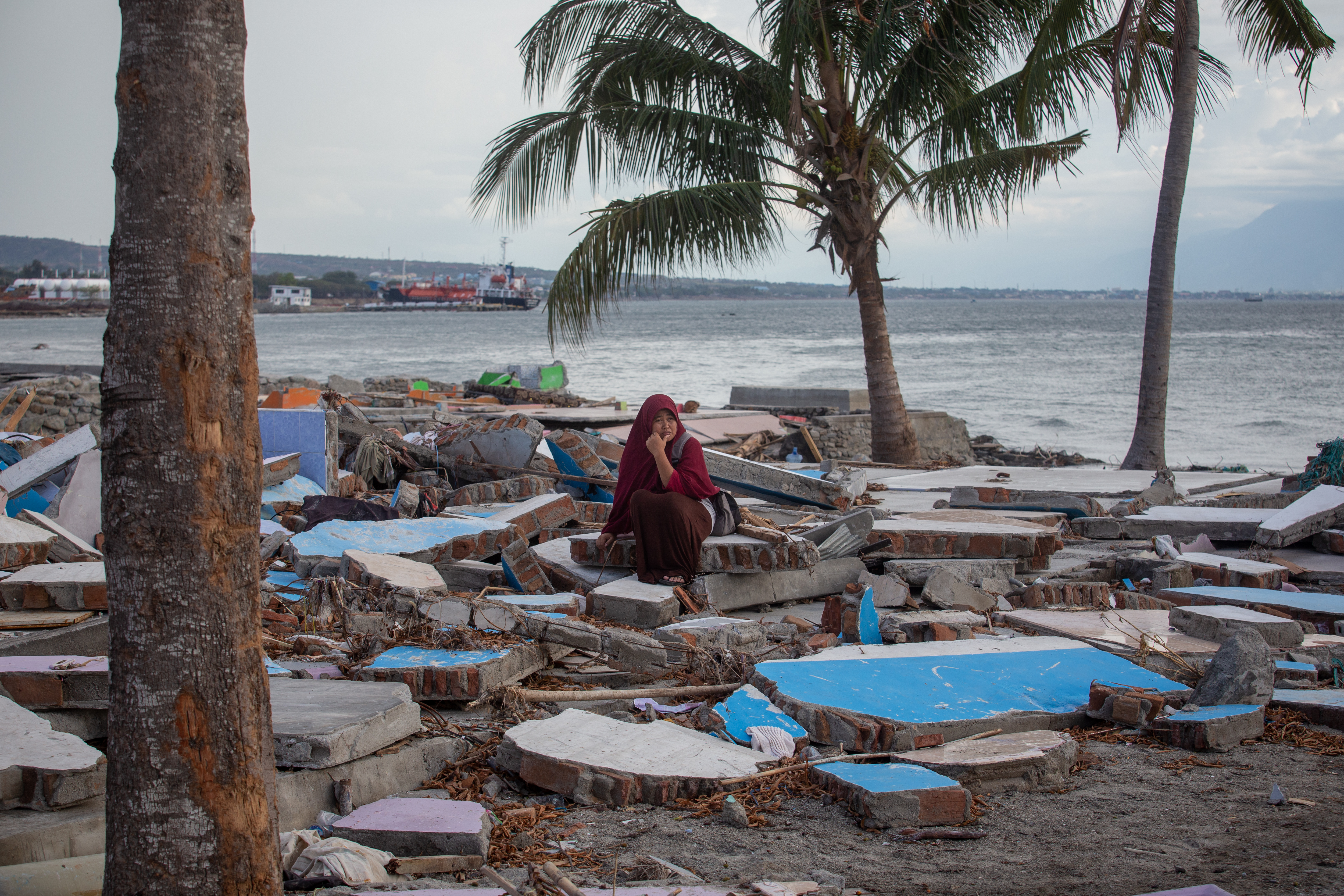 Eine Frau in Indonesien sitzt verzweifelt an einem Strand umgeben von Trümmern, nachdem das Erdbeben in Sulawesi einen Tsunami auslöste